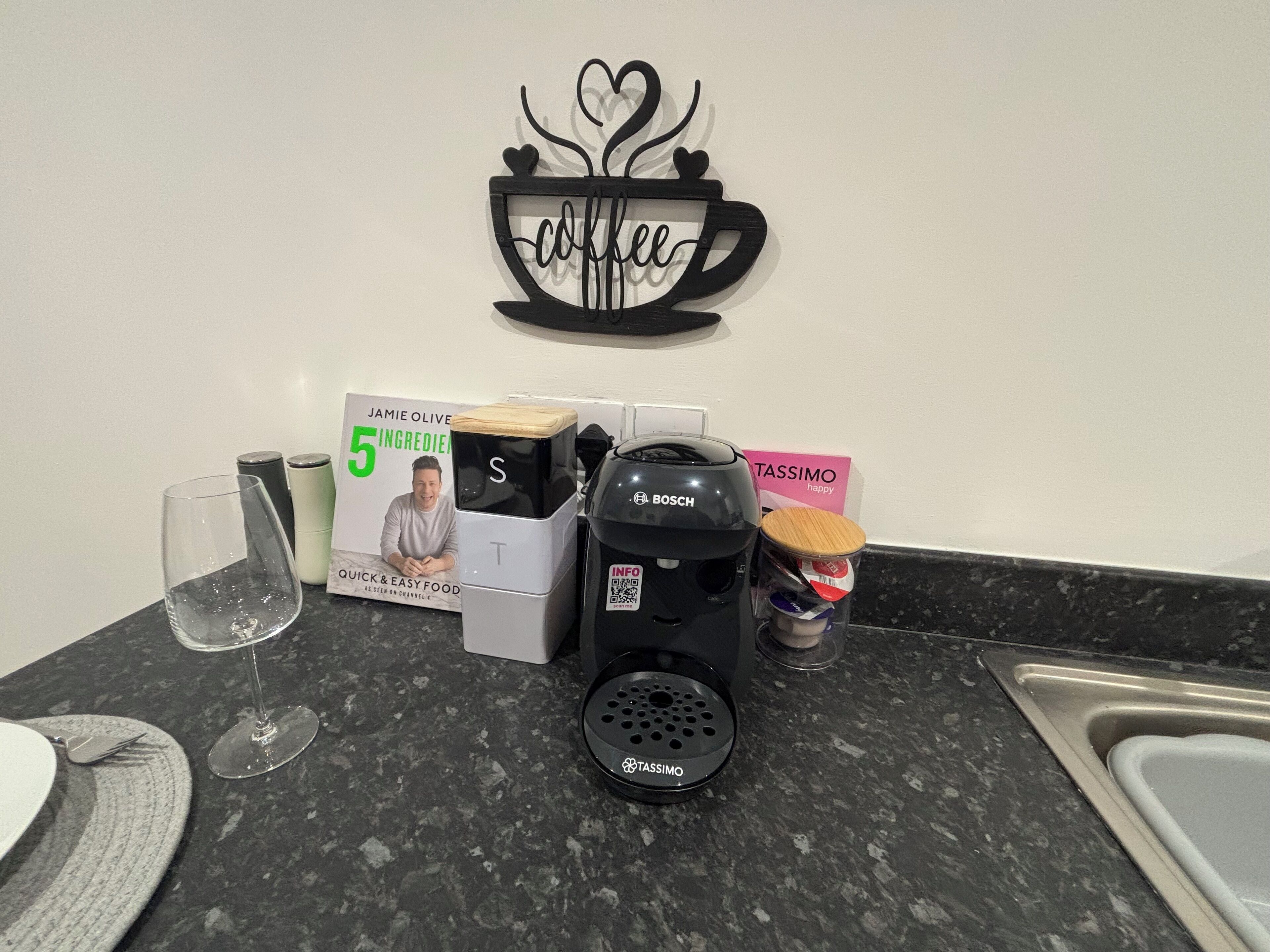 Eine Küchenarbeitsplatte mit einer Kaffeemaschine, einem Glas, einem Buch und einer Kaffeetasse.