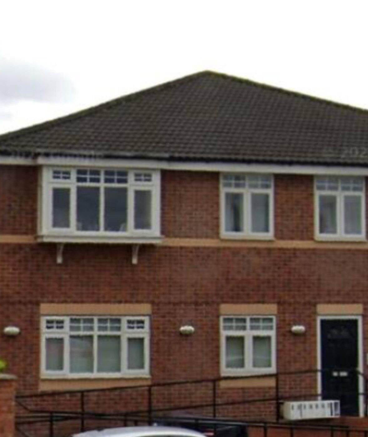 A two-story brick house with a tiled roof, multiple windows, and a black door.