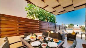 An outdoor dining area with wicker furniture and a table set for a meal, surrounded by a wooden fence and greenery. - Villa Marianna in Cape Greko with heated pool (Cape Greko)