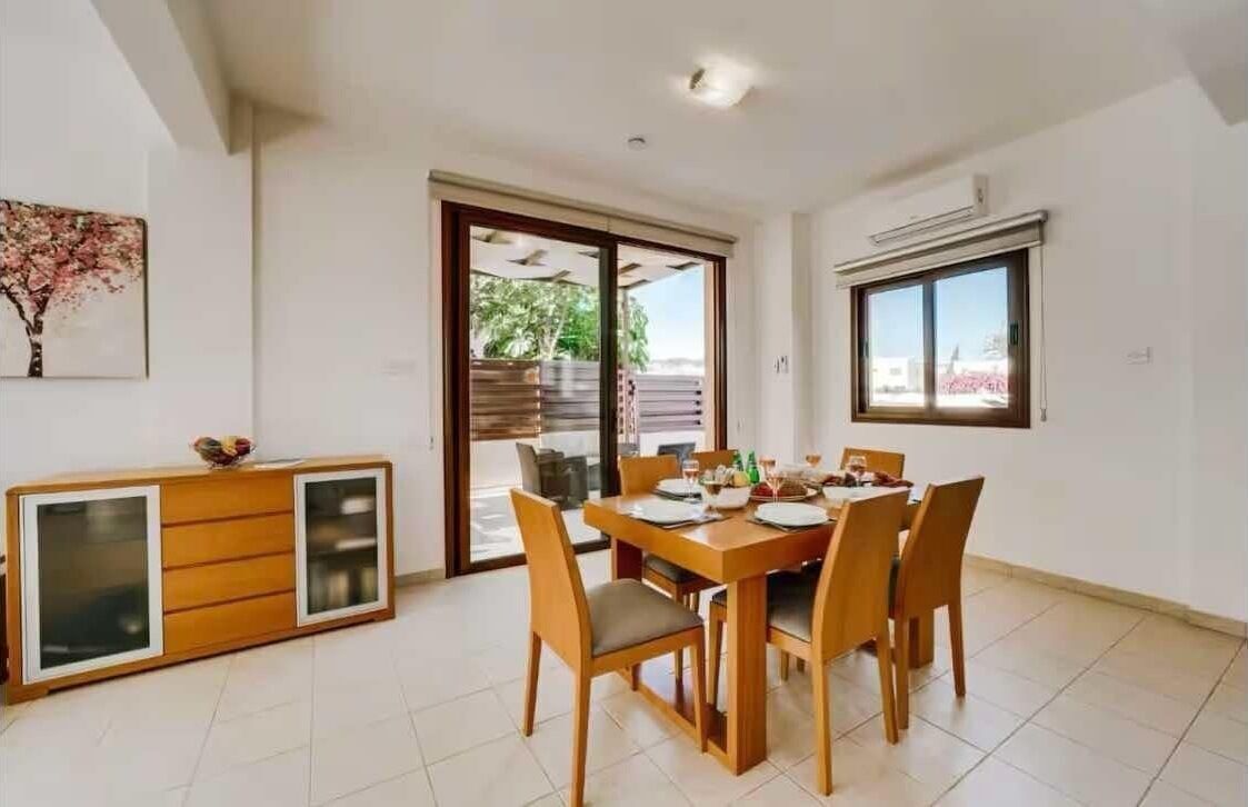 A dining area with a wooden table and chairs, a cabinet with glass doors, and a sliding glass door leading to an outdoor area.