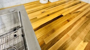 Une cuisine dotée d’un plan de travail en bois, d’un évier en acier inoxydable et d’un dosseret carrelé blanc.