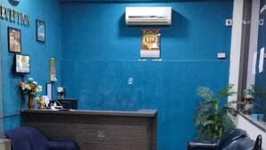 Ein Empfangsbereich mit blauer Wand, einer Rezeption, einer Uhr und einem Deckenventilator.