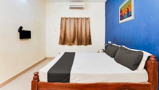 Ein Schlafzimmer mit einem hölzernen Bett, einem braunen Vorhang, einer Wandklimaanlage und einem Bild an der blauen Wand.