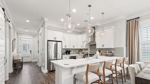 A modern kitchen with white cabinetry, a large island with bar stools, stainless steel appliances, and pendant lighting. - Free Shuttle to Beach, 3 Bedrooms Plus Loft, 30A Grayton Beach, Pool, Bikes (Santa Rosa Beach)