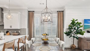A dining area with a wooden table, white upholstered chairs, and a chandelier. - Free Shuttle to Beach, 3 Bedrooms Plus Loft, 30A Grayton Beach, Pool, Bikes (Santa Rosa Beach)