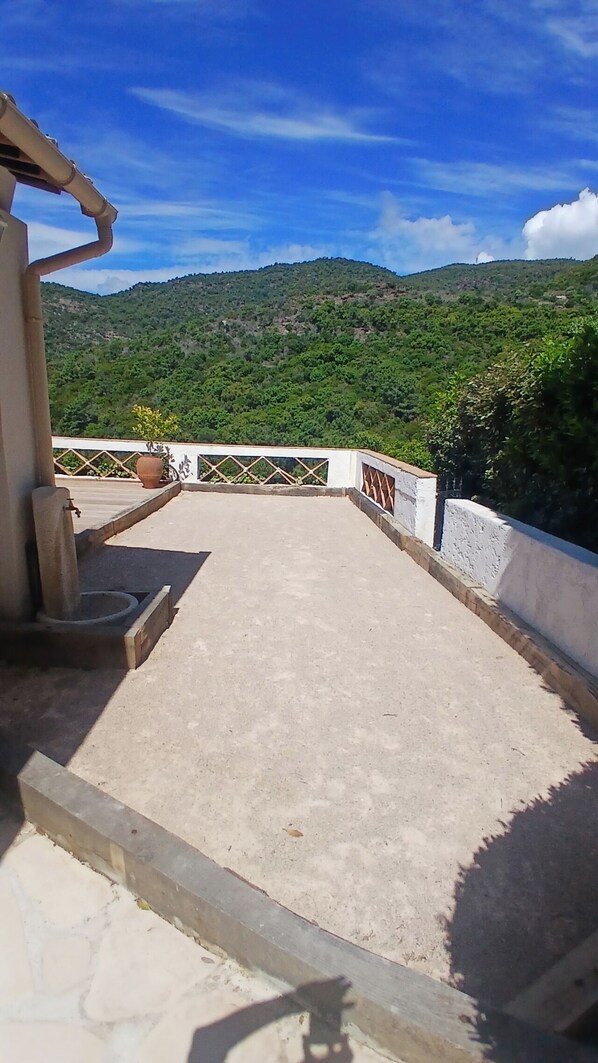 Una terraza en la azotea con suelo de hormigón, barandilla de metal y vistas a una colina verde.