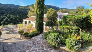 Un sendero de piedra conduce a un edificio con techo de tejas, rodeado de vegetación exuberante y un paisaje montañoso.