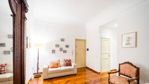 Amplia sala de estar con piso de parquet de madera, un sofá blanco, un sillón estampado y una lámpara de pie.