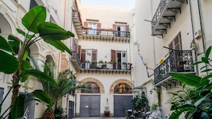 Un estrecho callejón con un edificio que tiene un balcón en el segundo piso con plantas y otro en el tercero con barandillas decorativas.