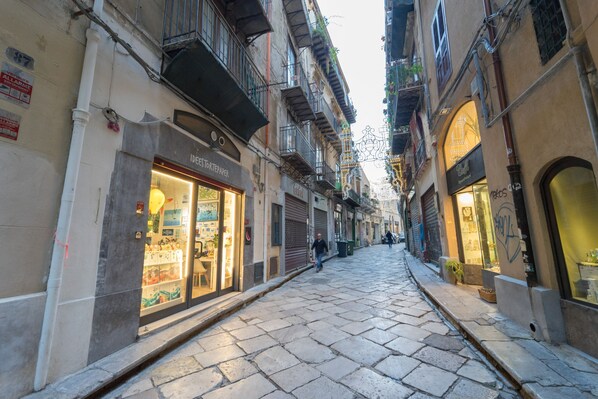 A narrow cobblestone street lined with multi-story buildings, some with balconies and storefronts. - Casa Marettu in Palermo (Palermo)