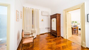Una habitación con suelo de parqué de madera, un radiador blanco, un armario de madera y una silla.