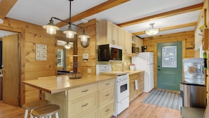 Cocina de cabaña de madera con mostrador de madera, electrodomésticos blancos y una puerta verde.