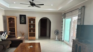 A living room with a sofa, wooden coffee table, two wooden shelves, a ceiling fan, and a TV on a wooden cabinet.