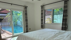 A bedroom with a bed, a window, and a view of a pool and greenery.