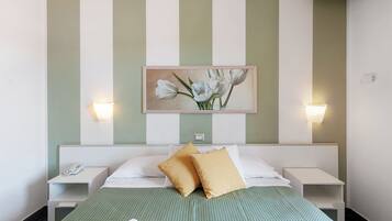 Habitació d'hotel amb llit, dues taules de nit, una petita taula auxiliar, una obra d'art floral emmarcada i llums penjades a la paret.