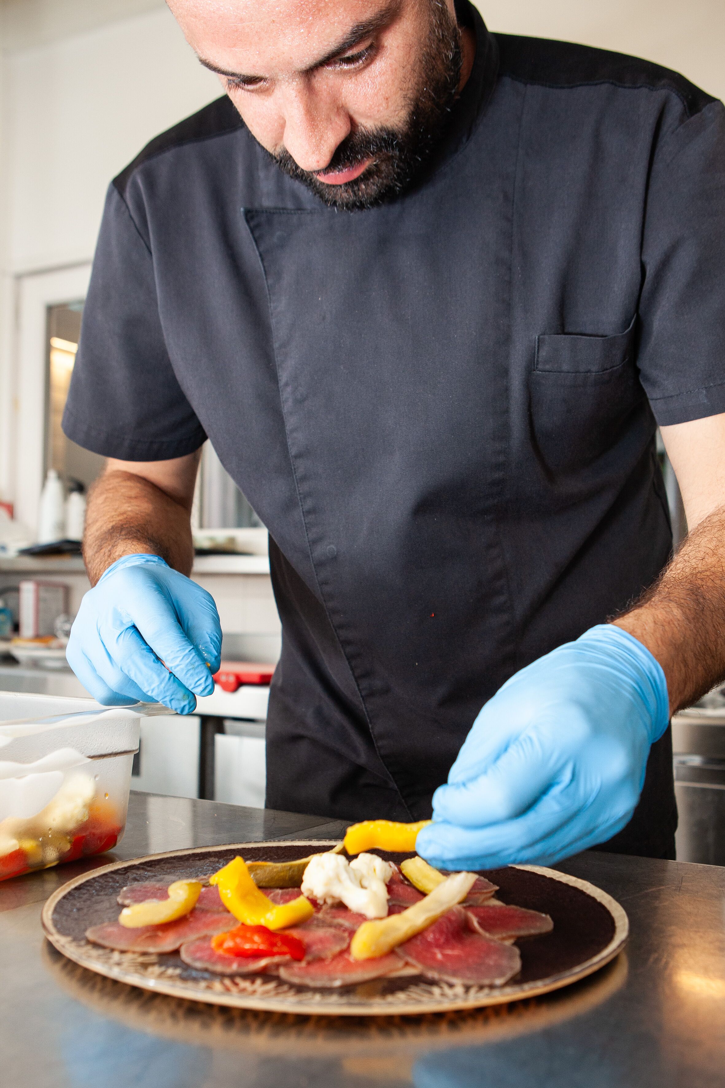 Una persona con uniforme negro y guantes azules preparando comida en un plato.
