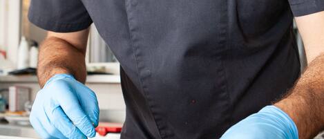 Una persona con uniforme negro y guantes azules preparando comida en un plato.