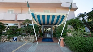 Entrada de hotel con toldo azul y blanco a rayas, pared de piedra y cartel de recepción.