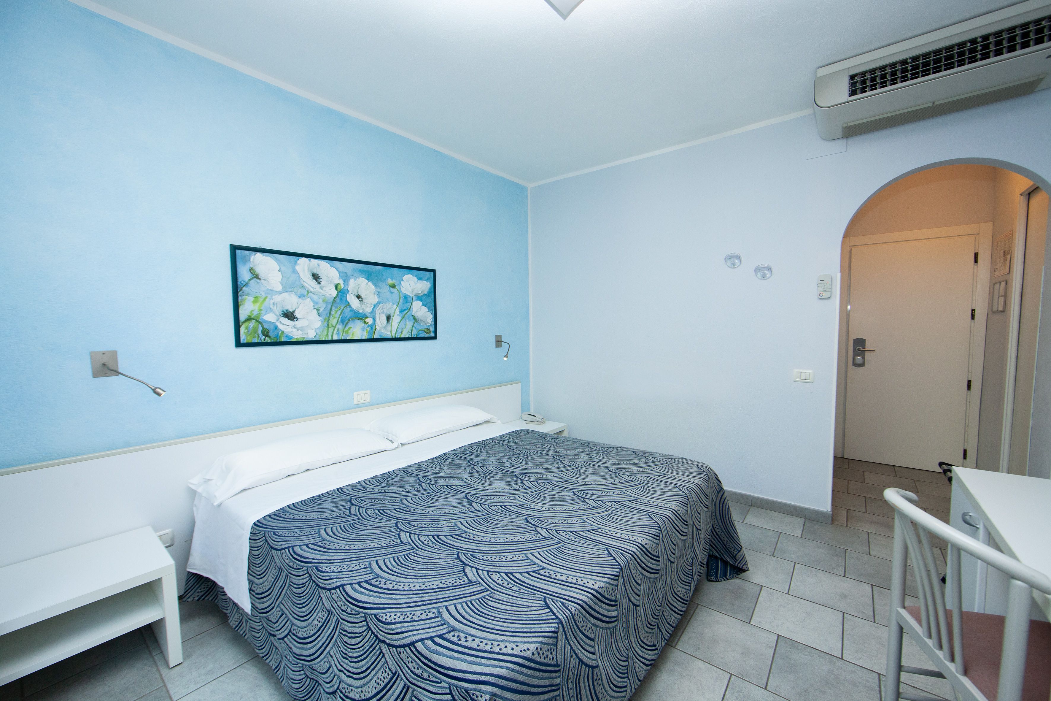 Een hotelkamer met een bed, een bureau, een schilderij en een deur.