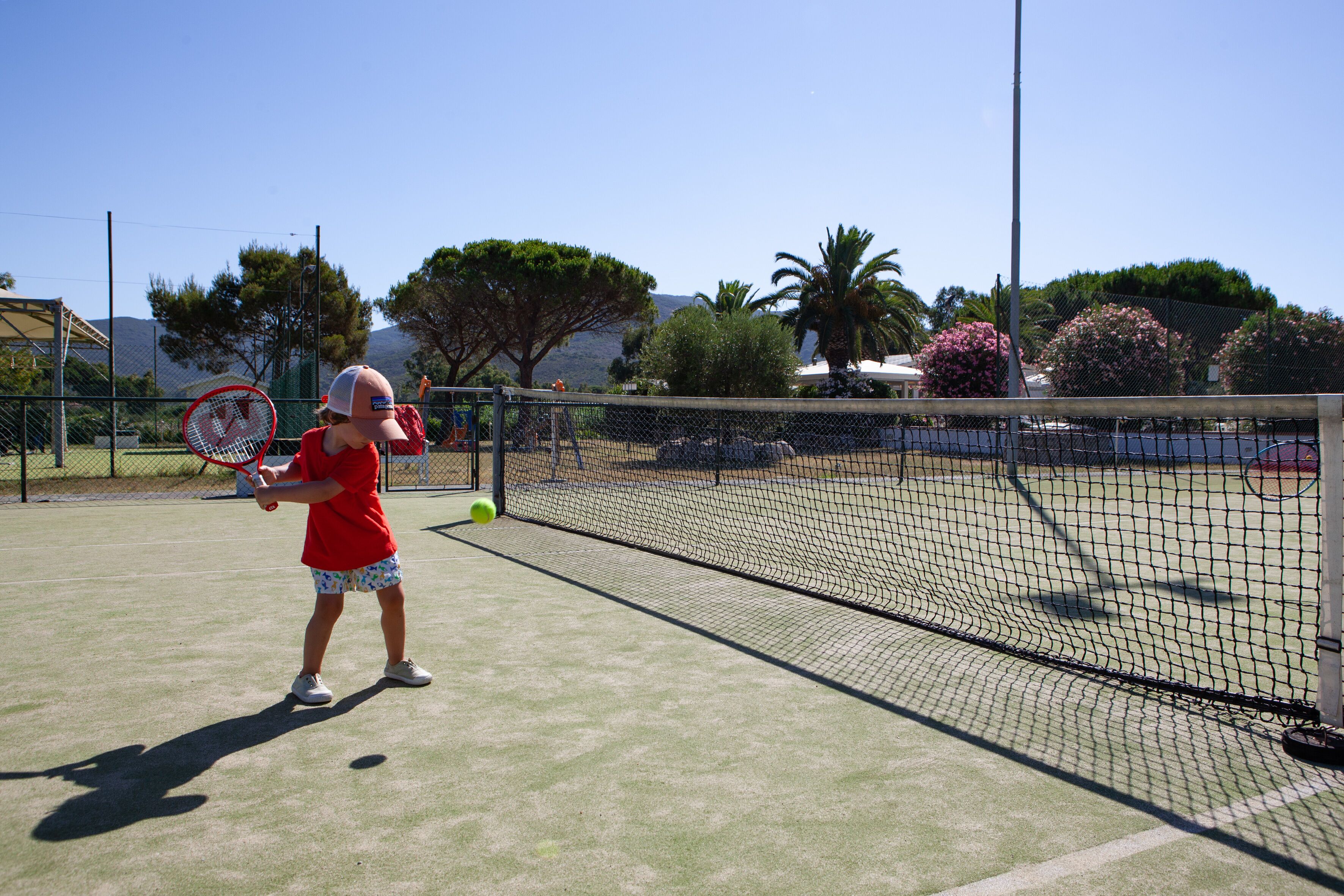 Un court de tennis avec un filet, un joueur portant un maillot rouge et une balle de tennis en mouvement.