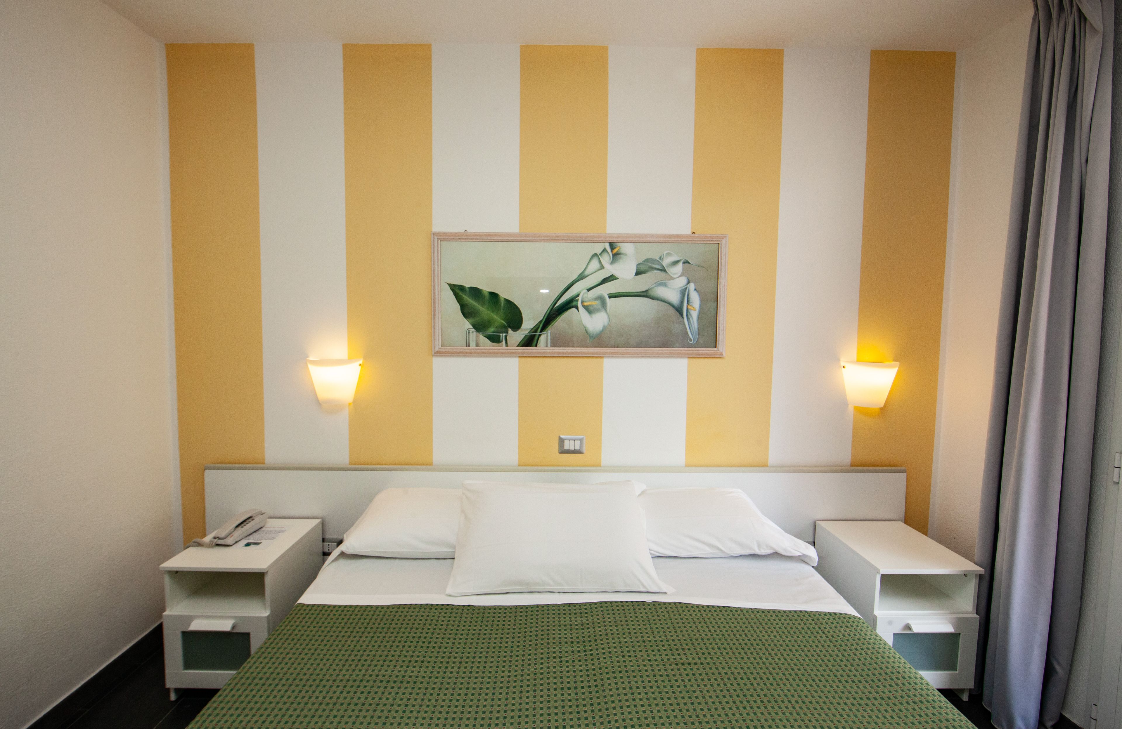 A hotel room with a bed, two bedside tables, a wall-mounted painting, and two wall-mounted lamps.