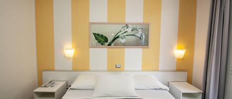 A hotel room with a bed, two bedside tables, a wall-mounted painting, and two wall-mounted lamps.