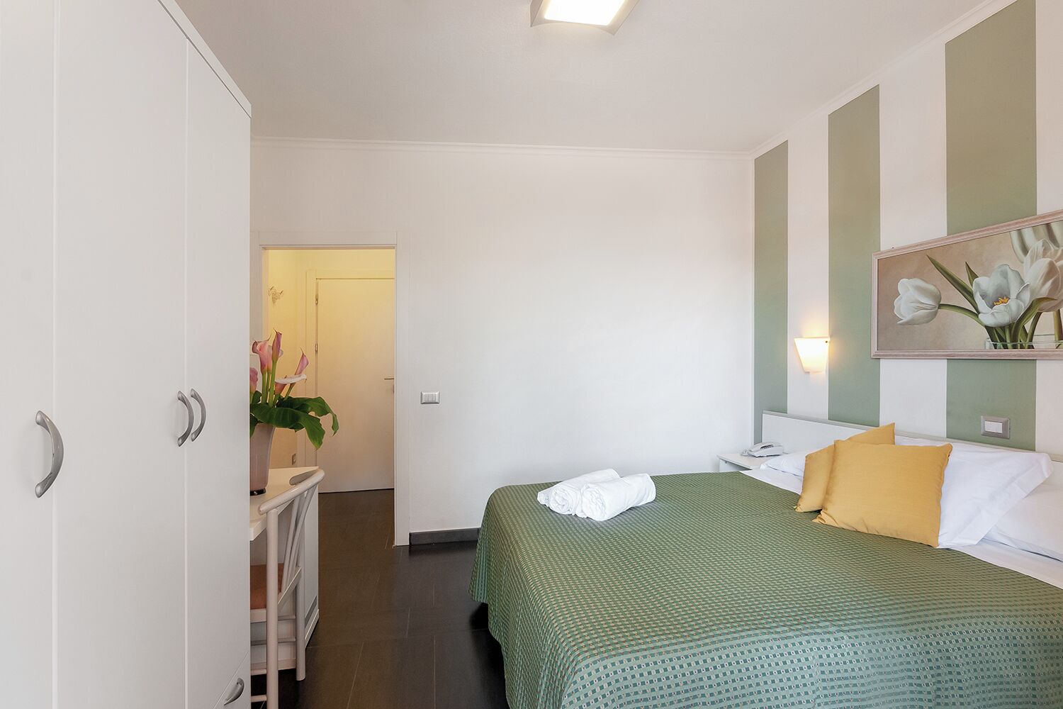 A hotel room with a bed, a bedside table, a mirror, and a wardrobe.