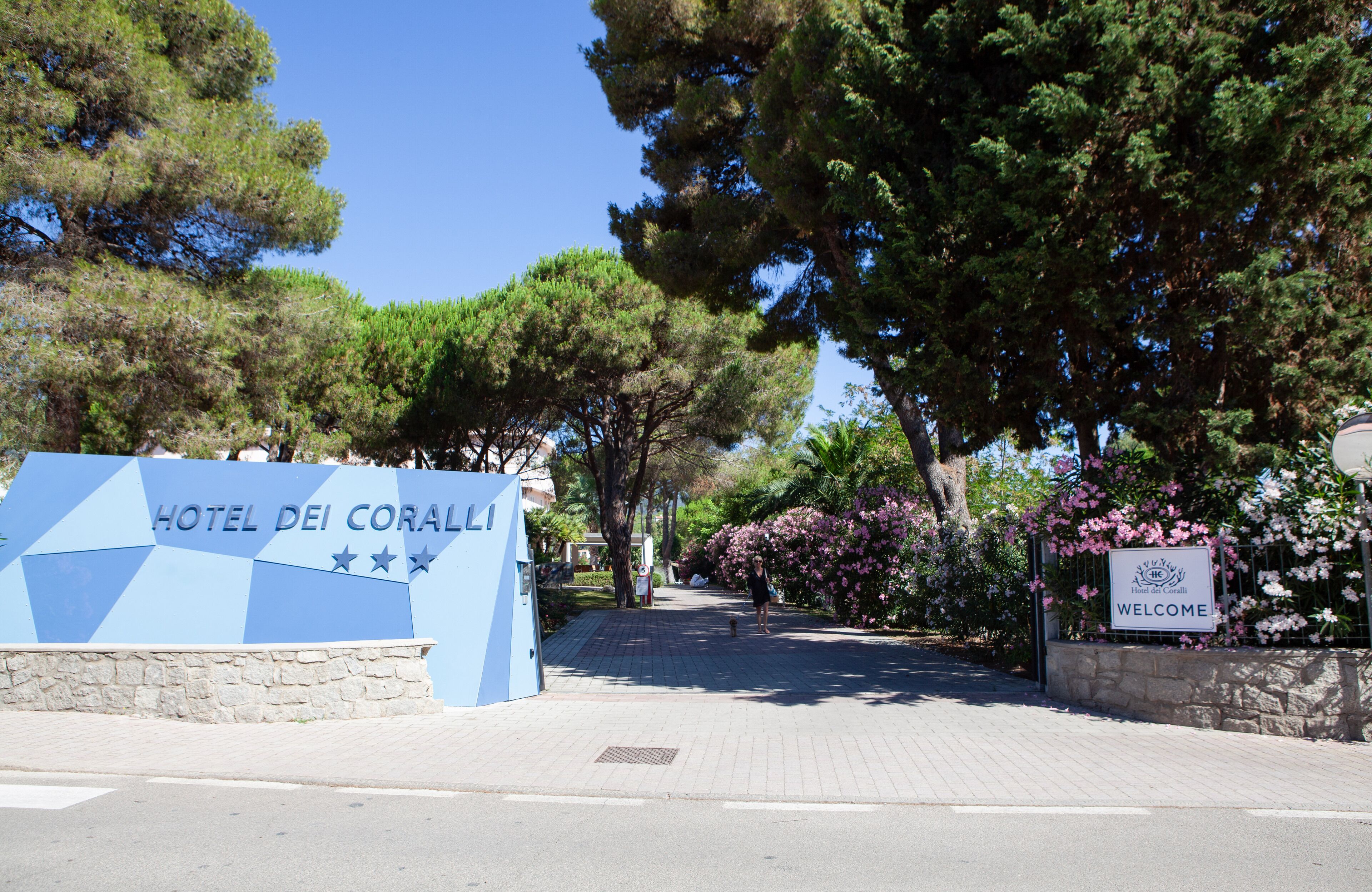 Entrada de un hotel con un letrero que dice "HOTEL DEI CORALLI" y un cartel de bienvenida.