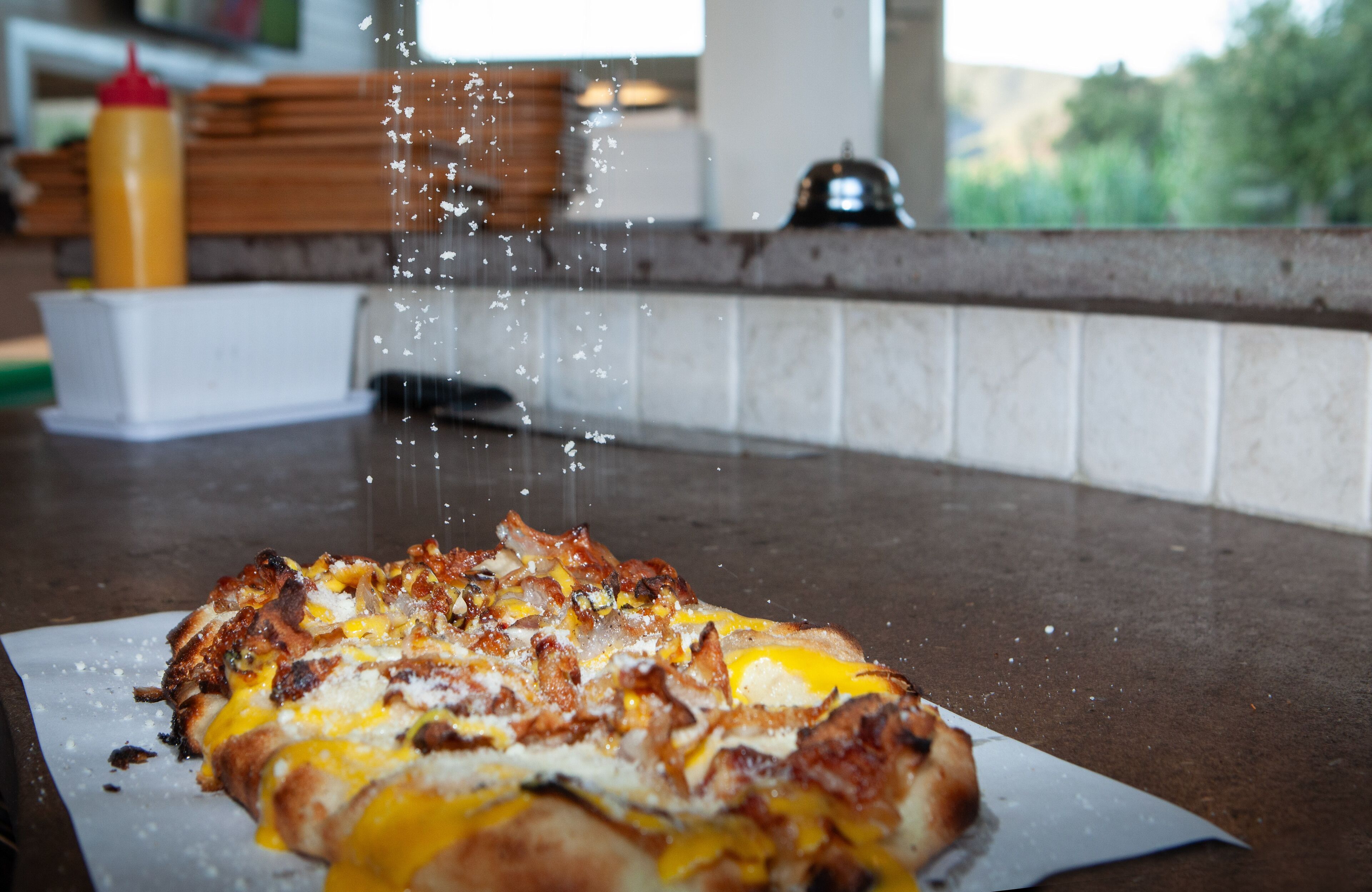 Una pizza en una bandeja con queso derretido y ingredientes, una botella de mostaza y una encimera de cocina.