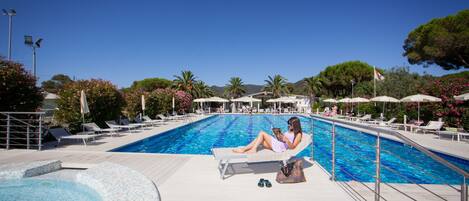 Un espace piscine avec des chaises longues et des parasols, une personne se relaxant sur une chaise, et un ciel bleu dégagé.