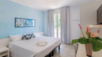 Una camera d'albergo con un letto, un comodino, una televisione, una finestra con tende e un quadro appeso al muro.