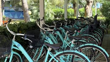 A row of turquoise bicycles parked in an outdoor area with greenery and trees in the background.