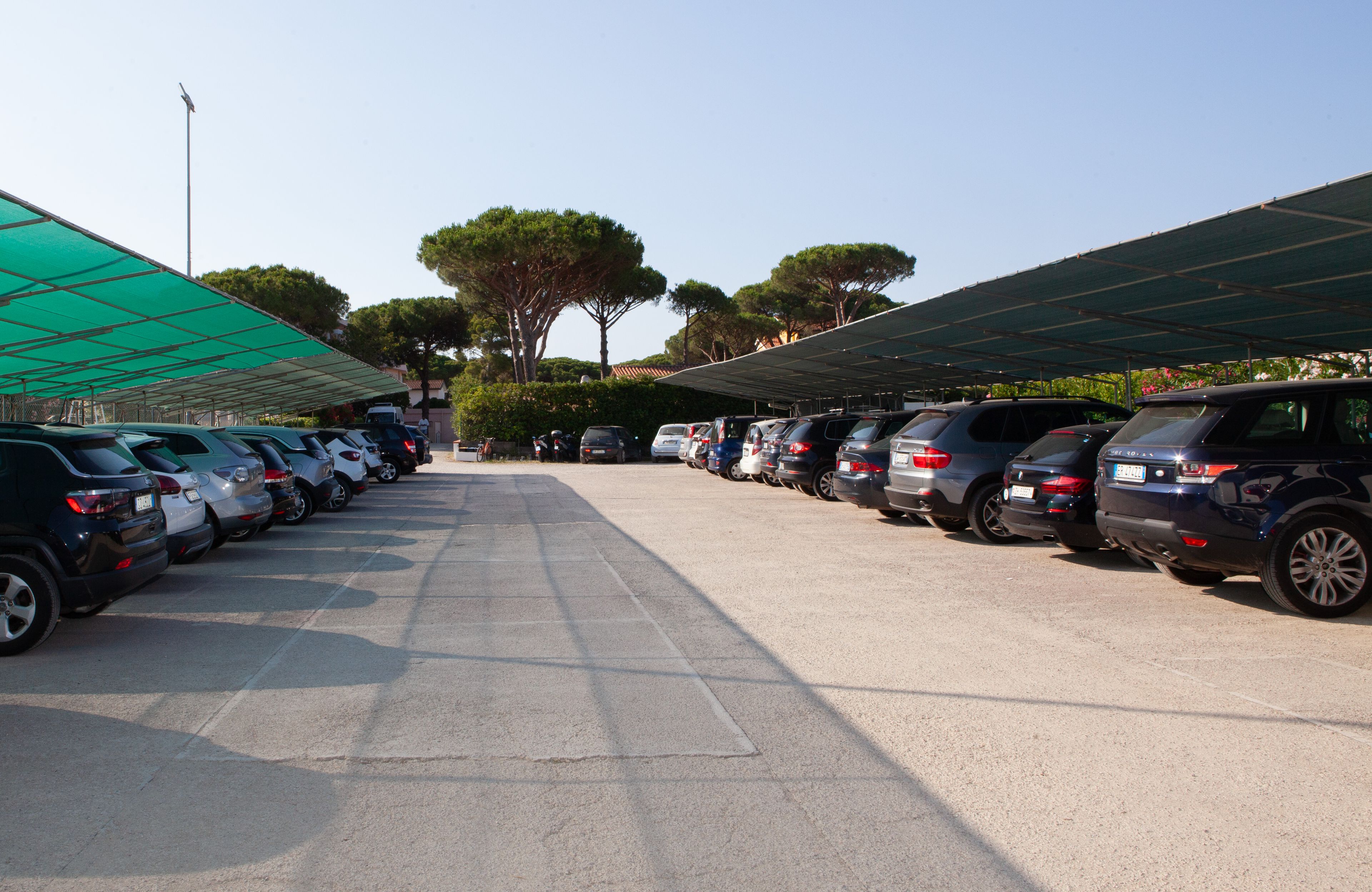 A parking lot with rows of parked cars under a large green canopy.