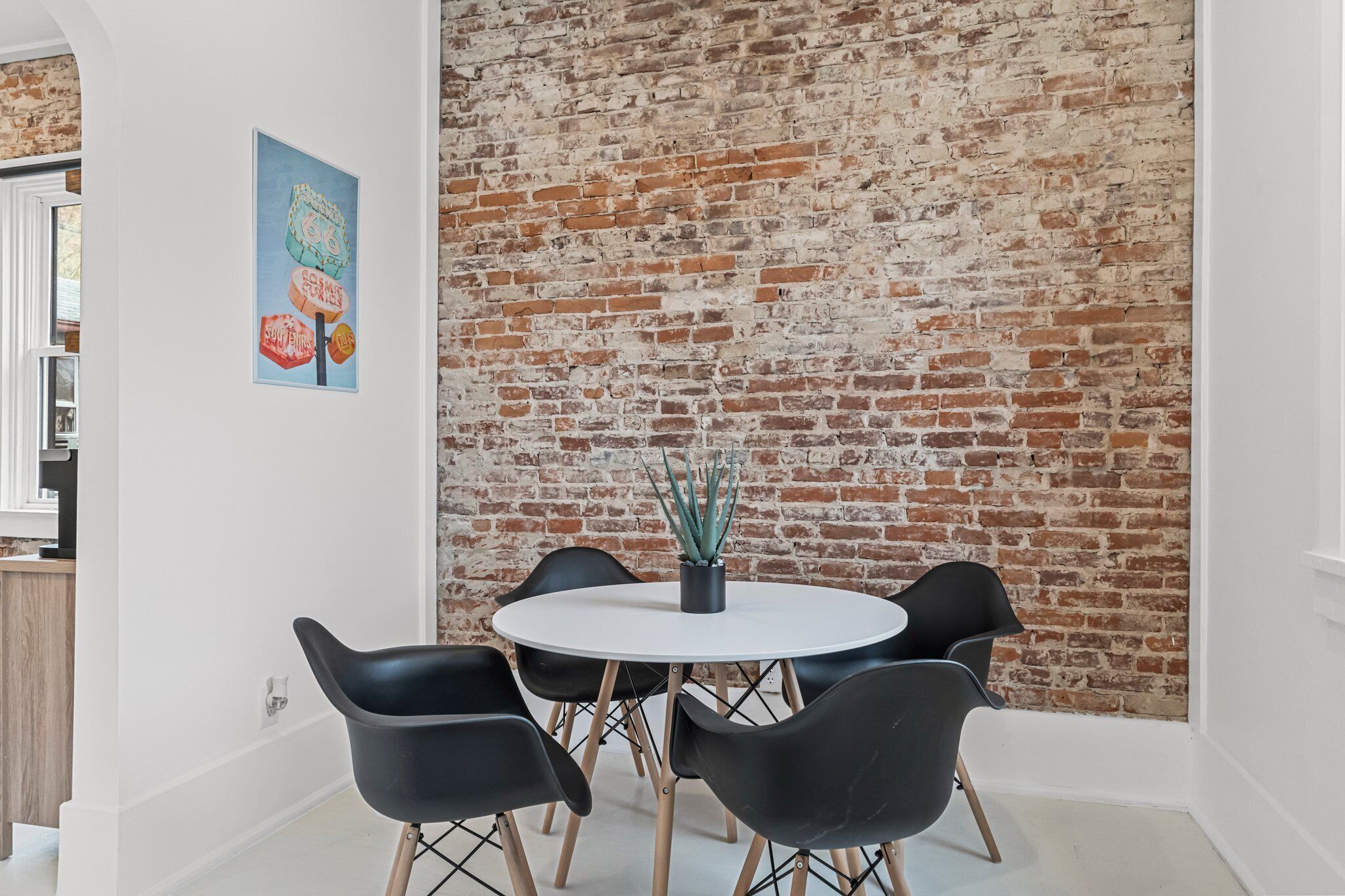 A dining area with a round table, black chairs, and a brick wall.
