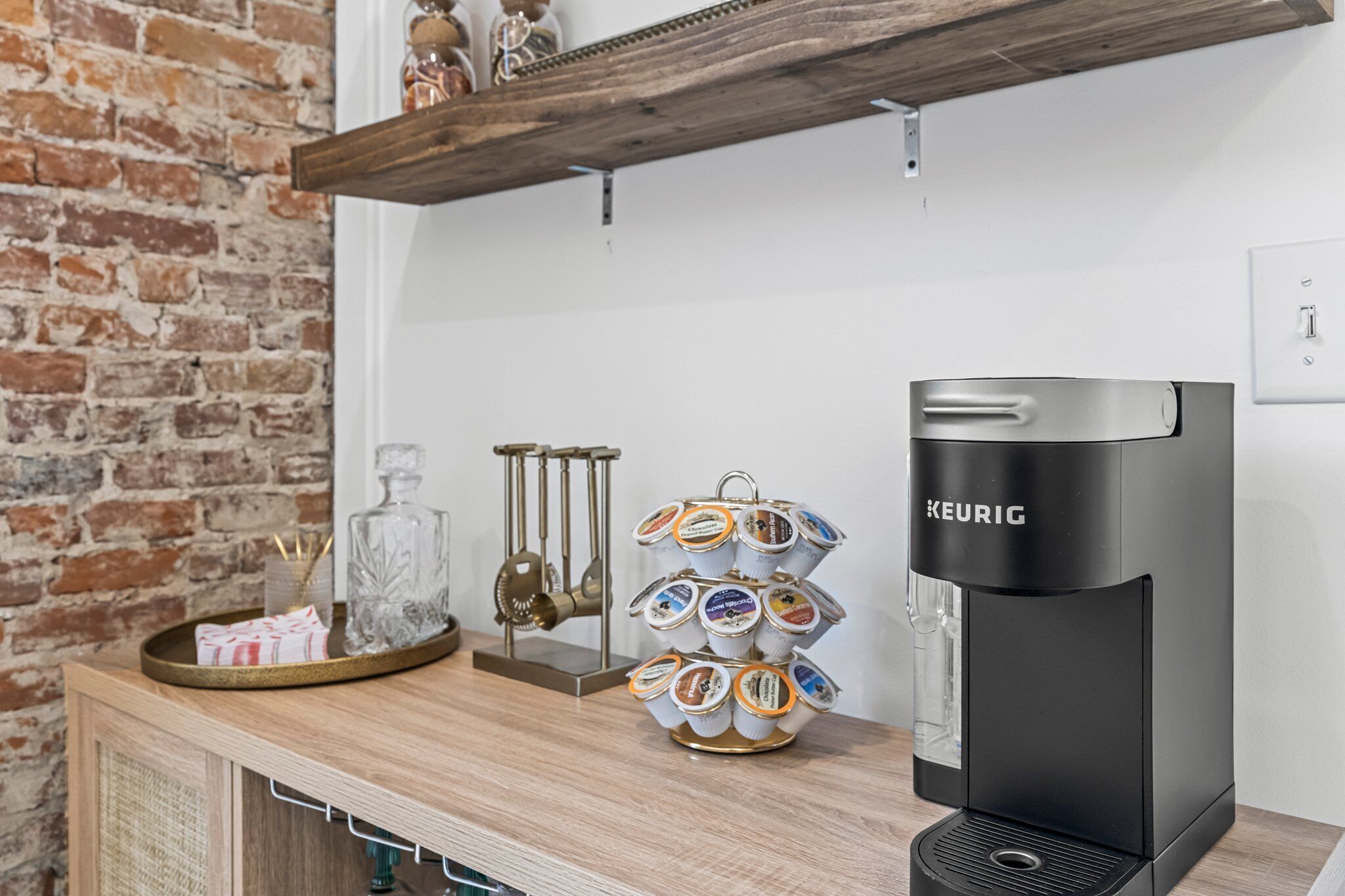 Una cocina moderna con una cafetera Keurig, un portacápsulas de café y una pared de ladrillo.