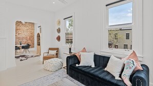 Een moderne woonkamer met een zwarte leren bank, een eethoek met een bakstenen muur, en een groot raam dat uitzicht biedt op buiten.