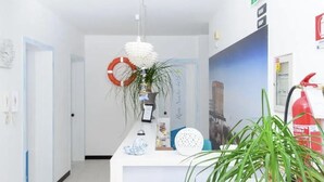 Un espace d’accueil avec un bureau blanc, une plante suspendue, un gilet de sauvetage et un extincteur.