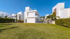 Un quartier résidentiel moderne avec des bâtiments blancs, une pelouse bien entretenue et des palmiers.