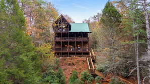 A cabin with a green roof, multiple decks, and a wooden staircase leading to the upper levels.