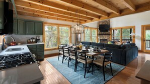 A spacious kitchen with wooden beams, a dining area with a large table and chairs, and a cozy living area with a sofa and fireplace.