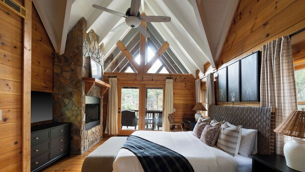 A bedroom with a large bed, wooden walls, stone accents, and a view through a glass door.