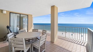 Ein Balkon mit Tisch und Stühlen, der auf einen Strand mit freiem Blick auf das Meer blickt.