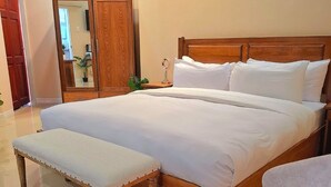 Un letto ben rifatto con lenzuola bianche, una testiera in legno e un comodino con uno specchio.