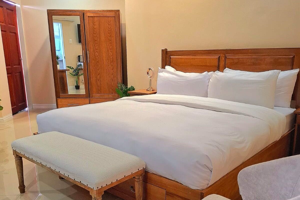 A neatly made bed with white linens, a wooden headboard, and a bedside table with a mirror.