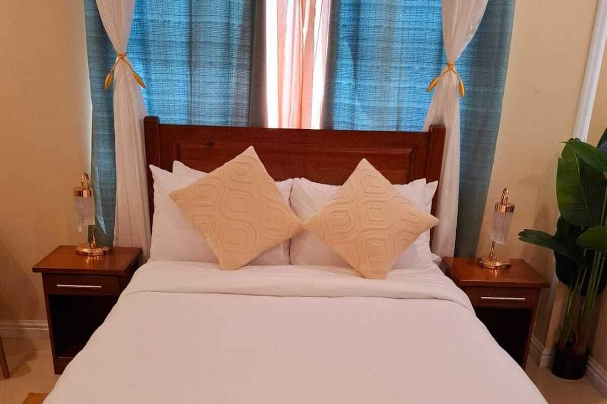 A neatly made bed with two pillows, a wooden headboard, and a bench at the foot of the bed.