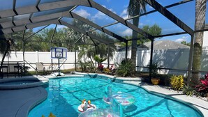 A swimming pool with inflatable toys, a covered patio, and a basketball hoop.