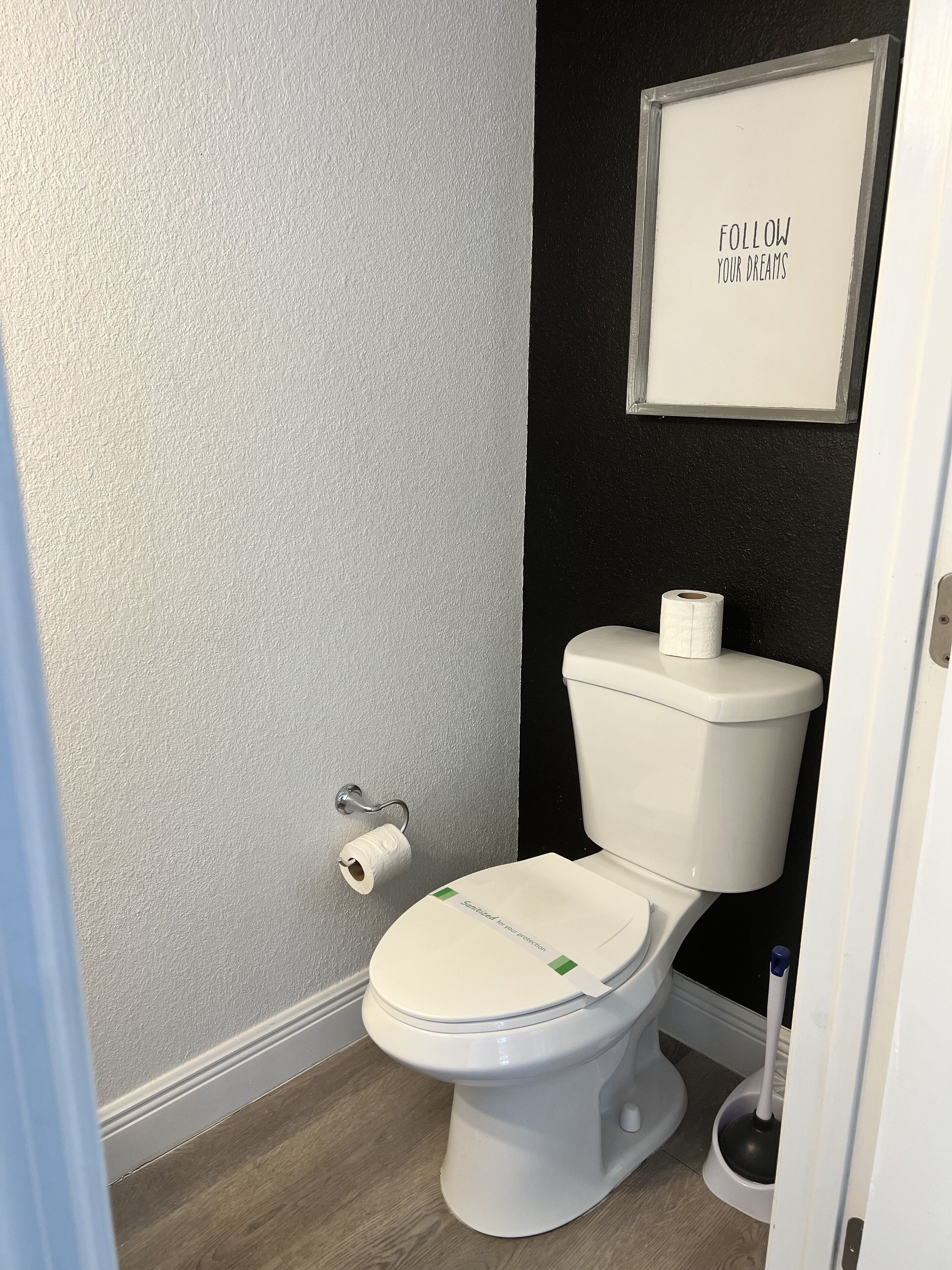 A small, modern bathroom with a toilet, a toilet paper holder, and a framed inspirational quote on the wall.