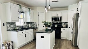 A modern kitchen with white cabinetry, a central island, a stainless steel refrigerator, and a microwave.