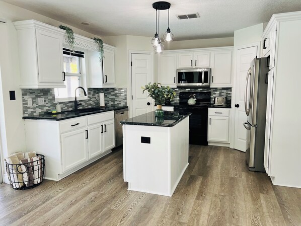 Una cocina moderna con armarios blancos, una isla central, un refrigerador de acero inoxidable y un microondas.