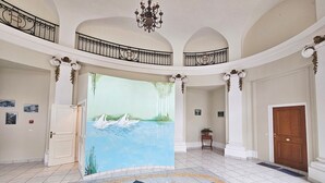 Eine geräumige Lobby mit einer großen Wandmalerei von Schwänen auf dem Wasser, einem prunkvollen Kronleuchter und einem sternförmigen Boden.